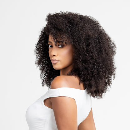 &quot;Model wearing a  afro or kinky texture wig with a side part. This wig is designed for alopecia, hair loss, fashion, or religious reasons. The wig features voluminous, bouncy curls and is showcased against a white studio background. The model has a natural, soft glam makeup look.