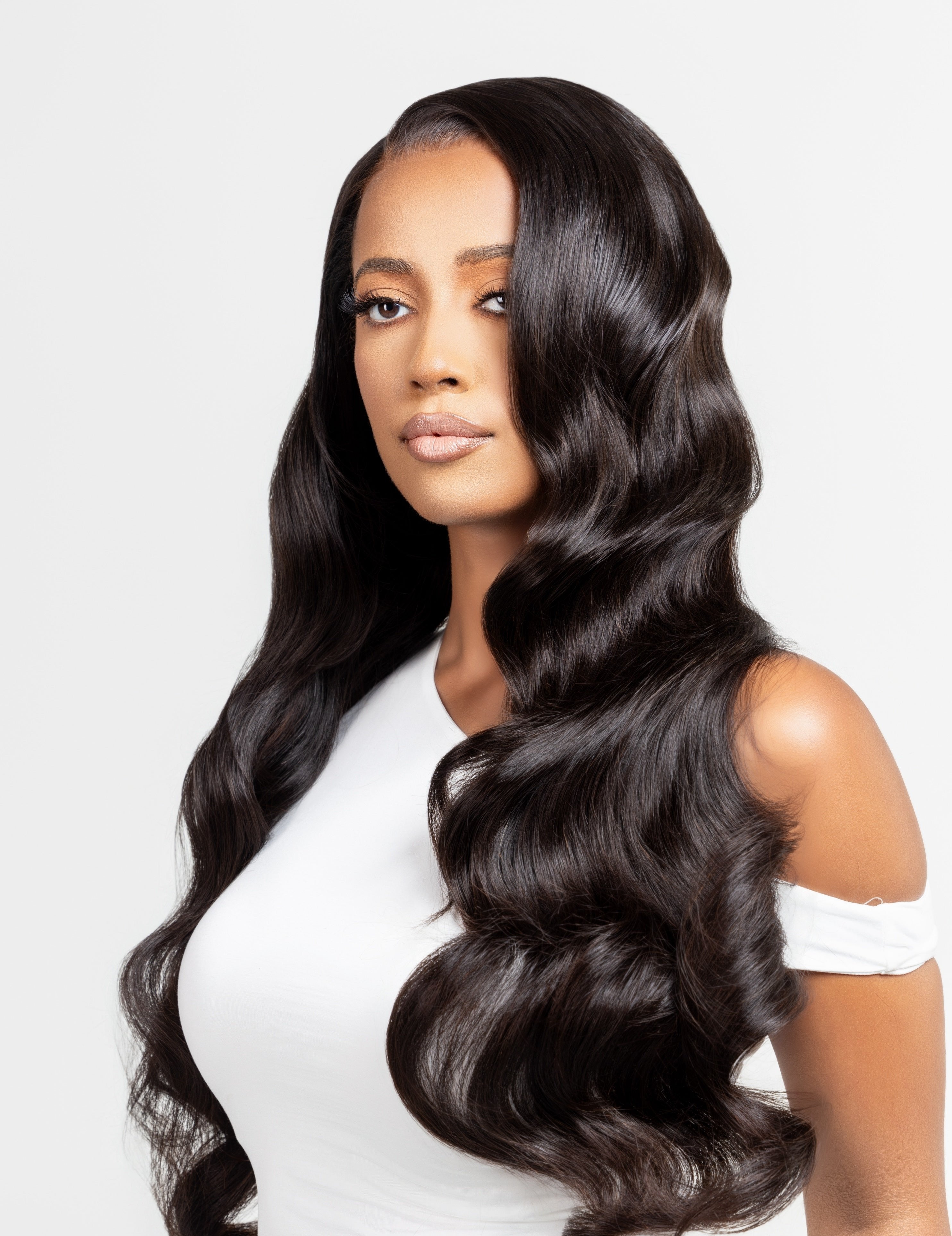 Model wearing a natural black wig with Hollywood waves, designed for alopecia, hair loss, fashion, or religious reasons. The wig features elegant, flowing curls and is styled against a white studio backdrop. The model&